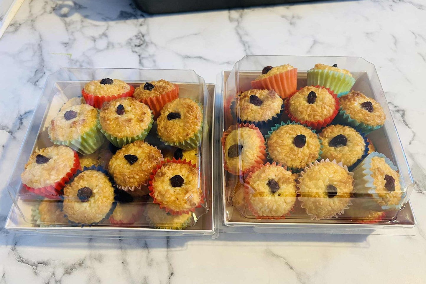 Two trays of colorful cupcakes with black decorations on a marble surface