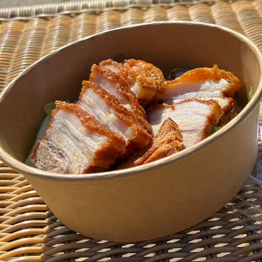 Bowl of Filipino lechon kawali on a wicker table with a blurred background