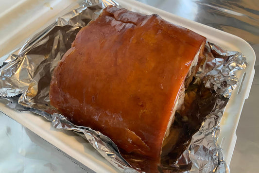 Roast pork on tin foil in a takeout container on a reflective surface